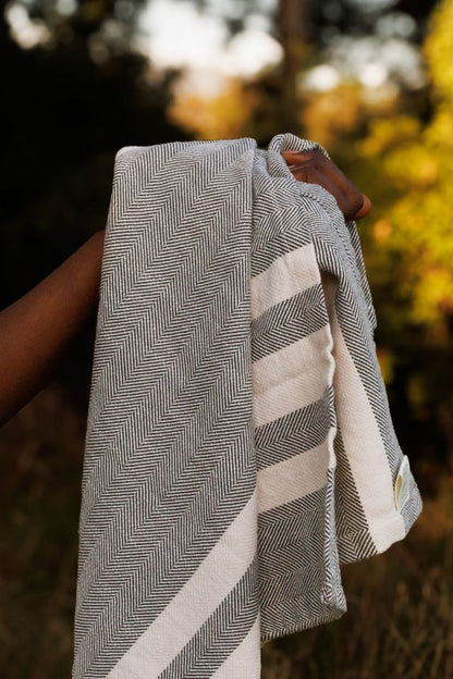 Person holding a gray and white striped towel outdoors with blurred natural background